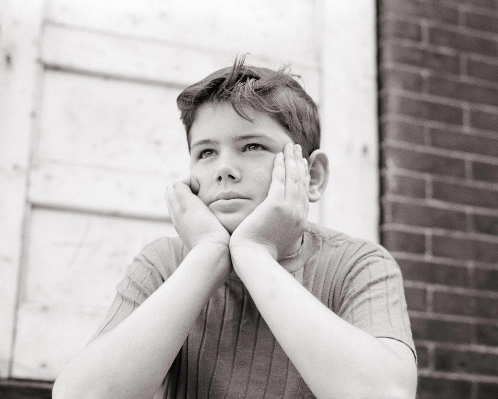 1960s SAD PRE-TEEN BOY SITTING BY OLD BRICK BUILDING RESTING HIS FACE IN HIS HANDS