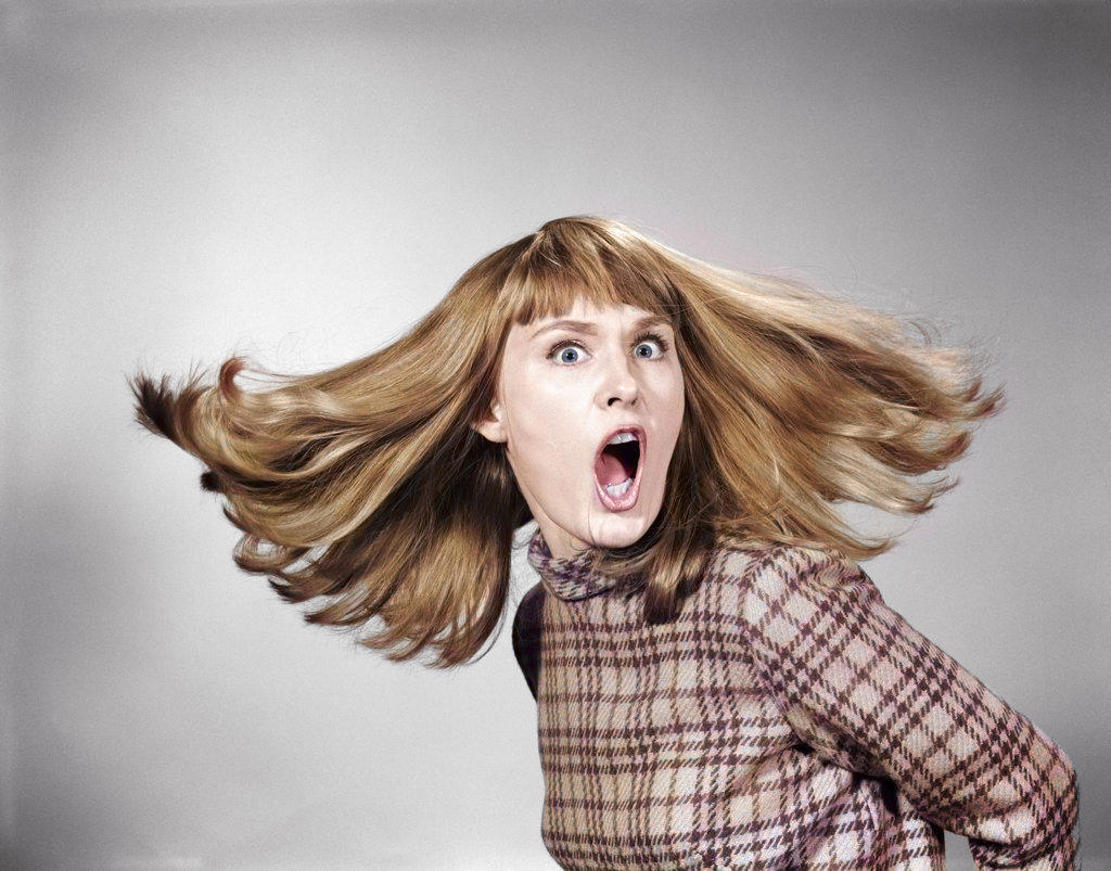 1960s PORTRAIT OF SURPRISED RED HAIR WOMAN LOOKING AT CAMERA WITH MOUTH WIDE OPEN AND HAIR FLYING