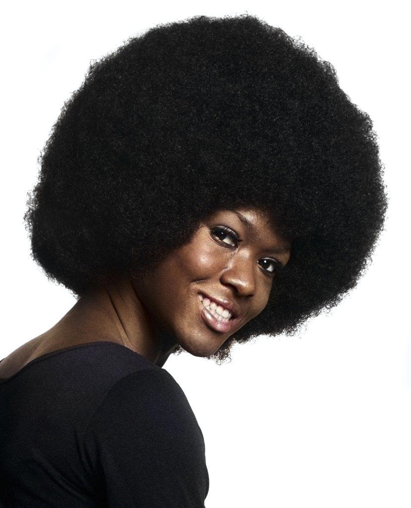 1970s PORTRAIT OF SMILING AFRICAN AMERICAN WOMAN WITH LARGE AFRO HAIR STYLE LEANING FORWARD LOOKING AT CAMERA OVER SHOULDER