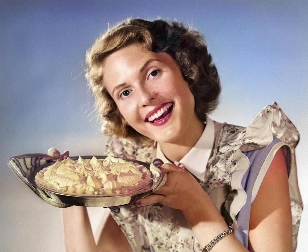 1950s SMILING WOMAN HOUSEWIFE WEARING APRON LOOKING AT CAMERA PRESENTING HOLDING FRESHLY BAKED MERINGUE TOP PIE