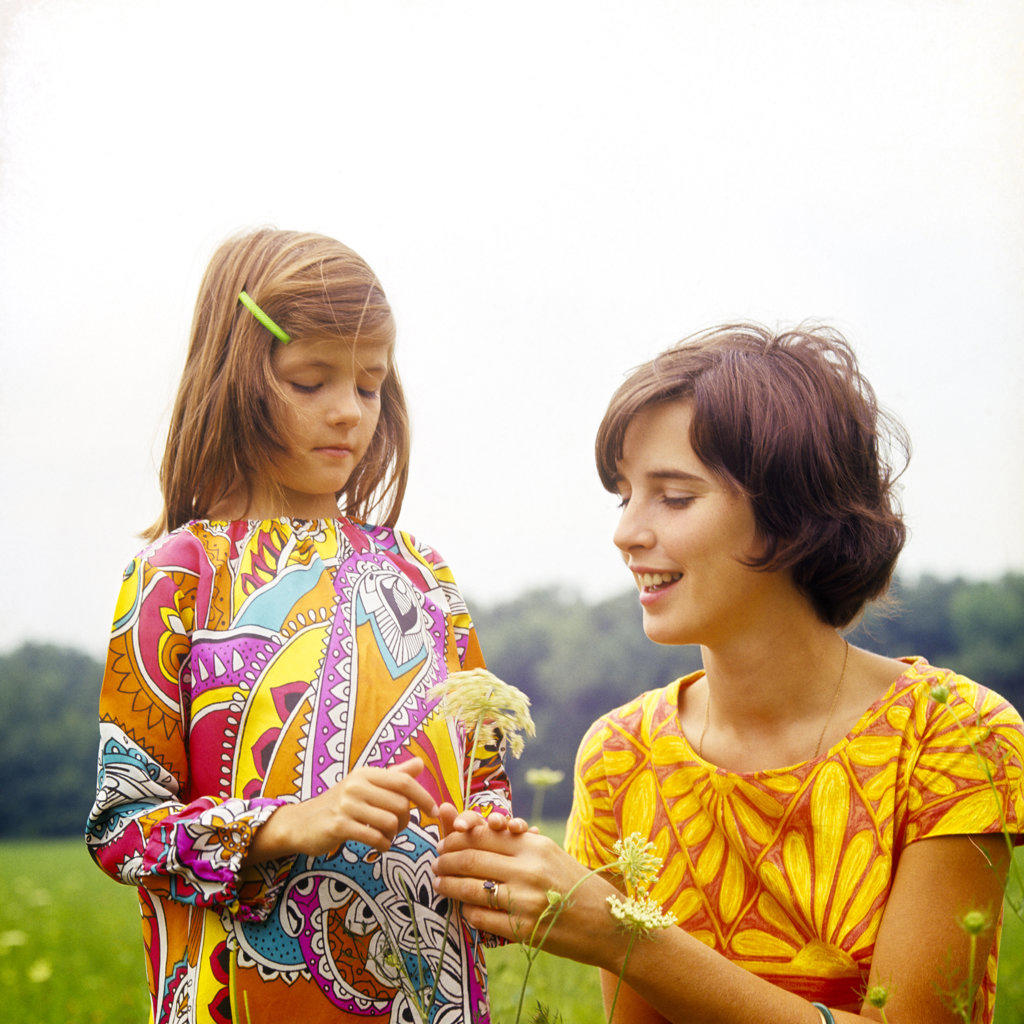1960s 1970s BRUNETTE MOTHER AND CURIOUS DAUGHTER WEARING PRINT DRESSES OUTDOOR EXAMINING PICKING QUEEN ANNE’S LACE WILD FLOWER