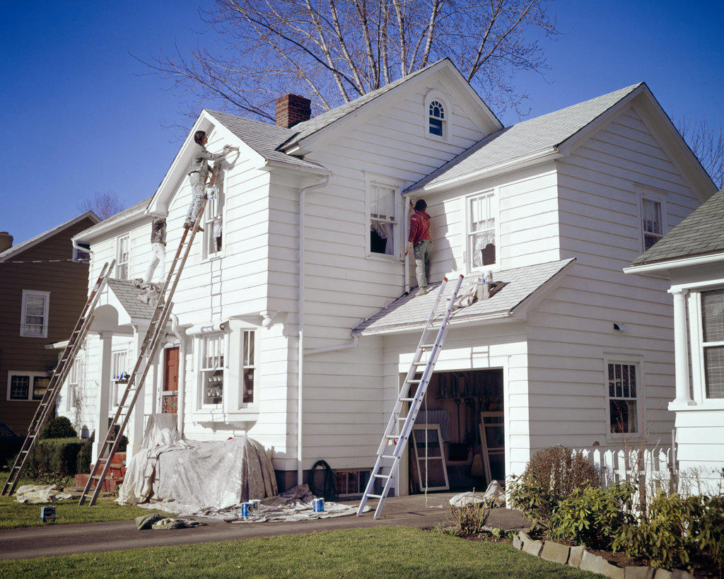 1970s FOUR MEN PROFESSIONAL CREW PAINTING THE EXTERIOR OF A WHITE WOODEN CLAPBOARD TWO STORY SUBURBAN HOUSE