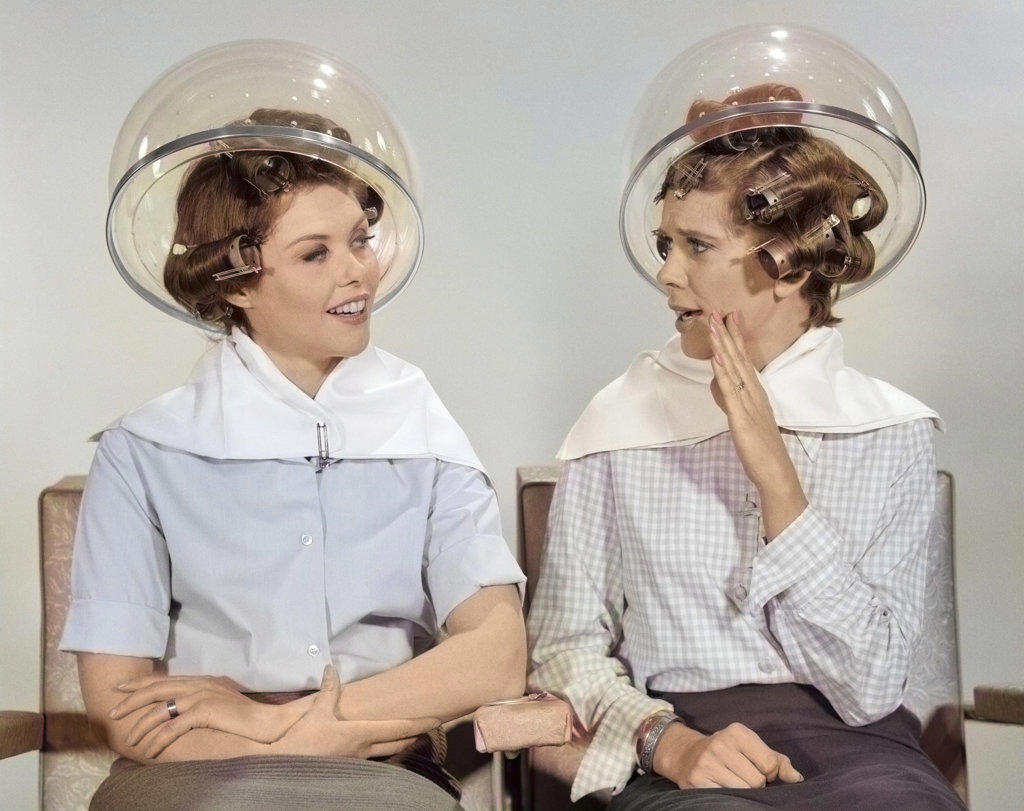 1960s TWO WOMEN SITTING TOGETHER GOSSIPING UNDER HAIRDRESSER HAIR DRYER