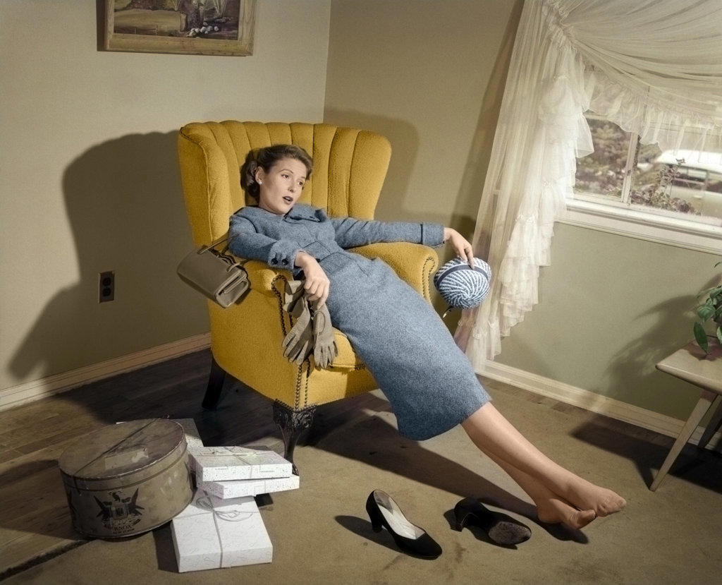 1950s EXHAUSTED TIRED WOMAN SLUMPED IN LIVING ROOM CHAIR WITH SHOES OFF AT HOME RECOVERING AFTER RETURNING FROM SHOPPING TRIP