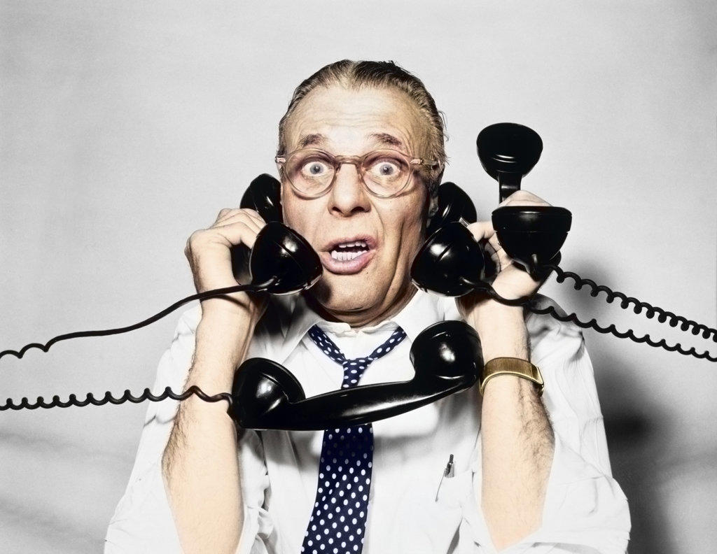 1950s 1960s PORTRAIT OF FRAZZLED BUSINESSMAN TRYING TO ANSWER FOUR BLACK TELEPHONES PHONES AT ONCE