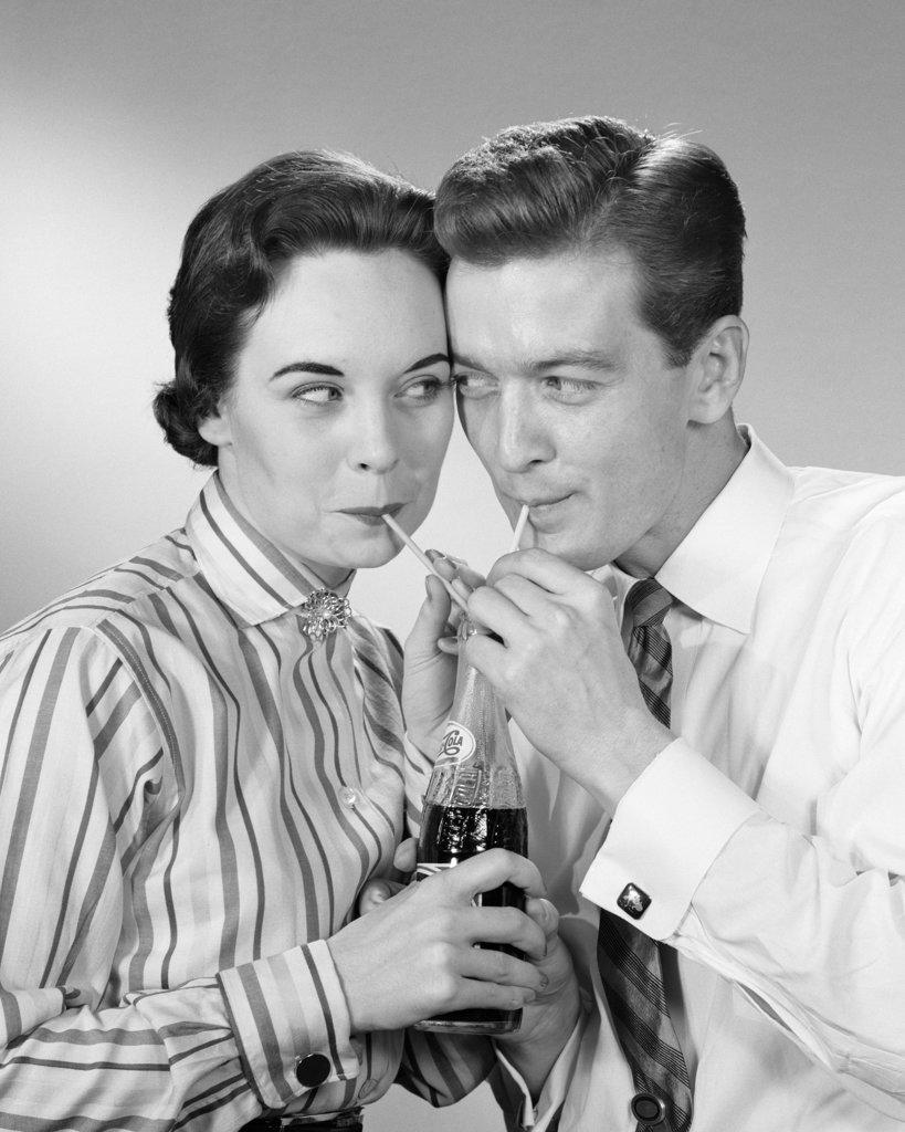 1950s ROMANTIC COUPLE HEAD TO HEAD SHARING A SODA POP COLA ONE BOTTLE TWO STRAWS