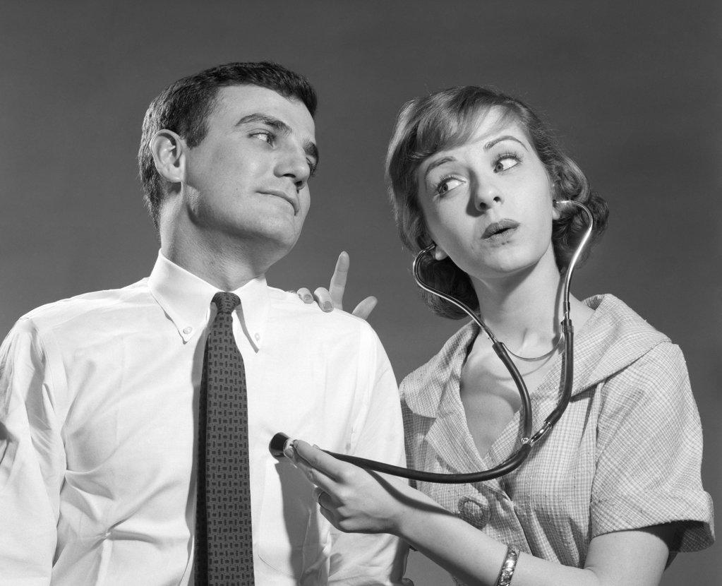 1960s WIFE WITH STETHOSCOPE ON HUSBAND 