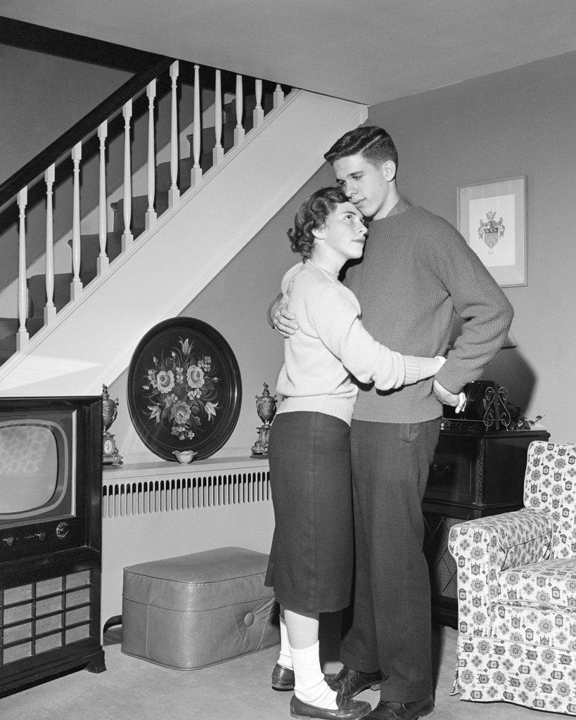 1950s HUGGING DANCING TEENAGE COUPLE IN LIVING ROOM