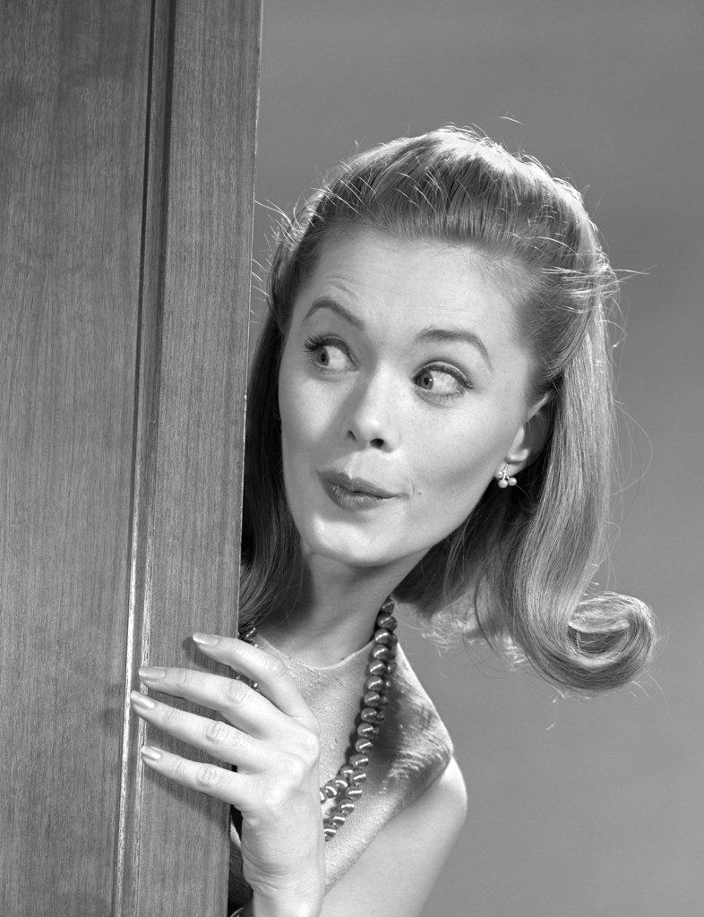 1960s WOMAN PEEKING AROUND DOOR WITH FUNNY FACIAL EXPRESSION