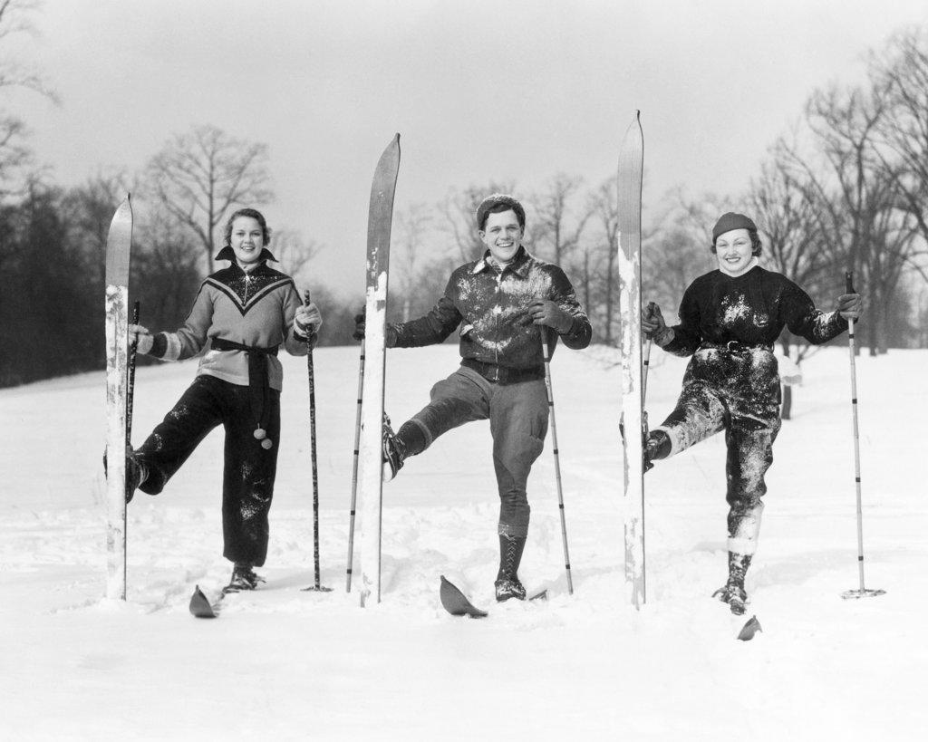 1930s TWO WOMEN AND A MAN LOOKING AT CAMERA SMILING POSING ON SKIS WITH RIGHT SKI TURNED UPRIGHT 