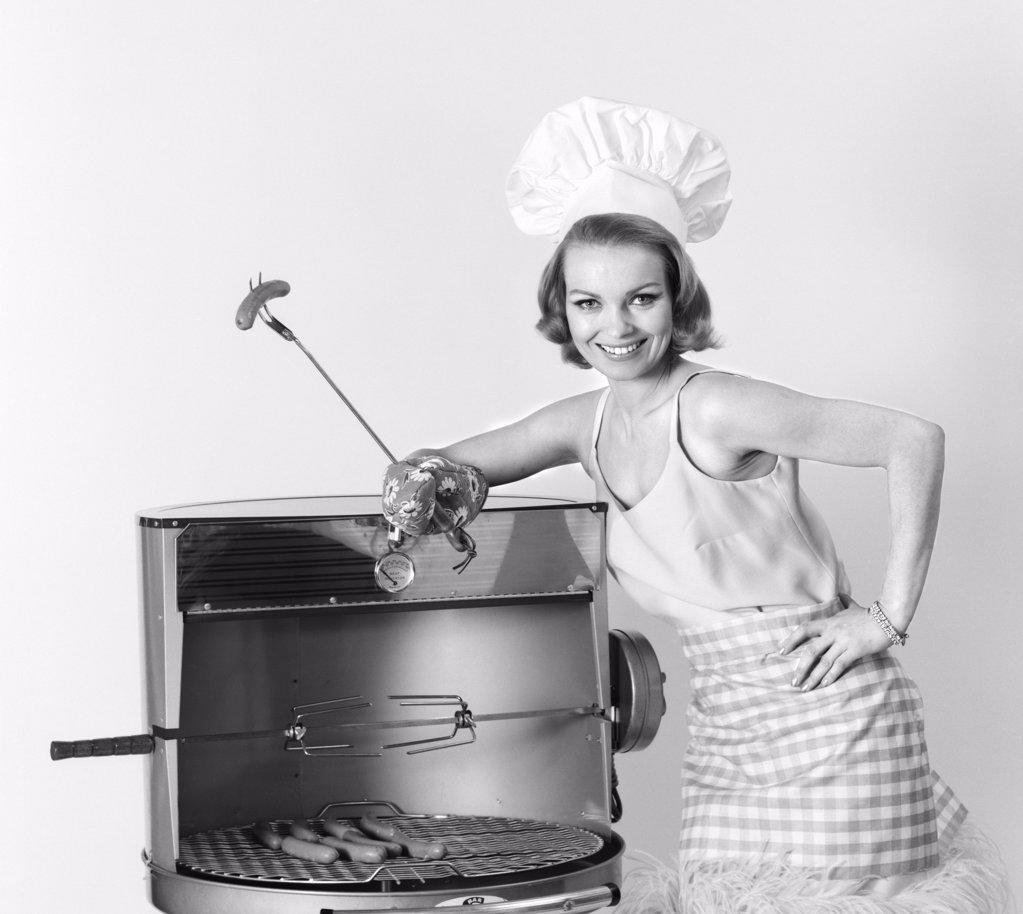 1960S Woman Wearing Chef Hat Standing At Bbq Grill Holding A Fork With Hot Dog