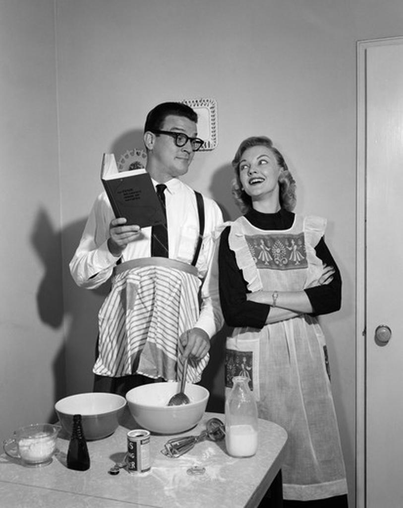 1950S Couple In Kitchen With Husband Learning To Cook While Wife Watches
