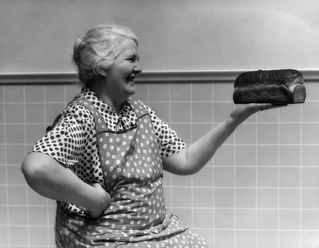 1930S 1940S Grandmother In Apron Admiring Loaf Of Freshly Baked Bread