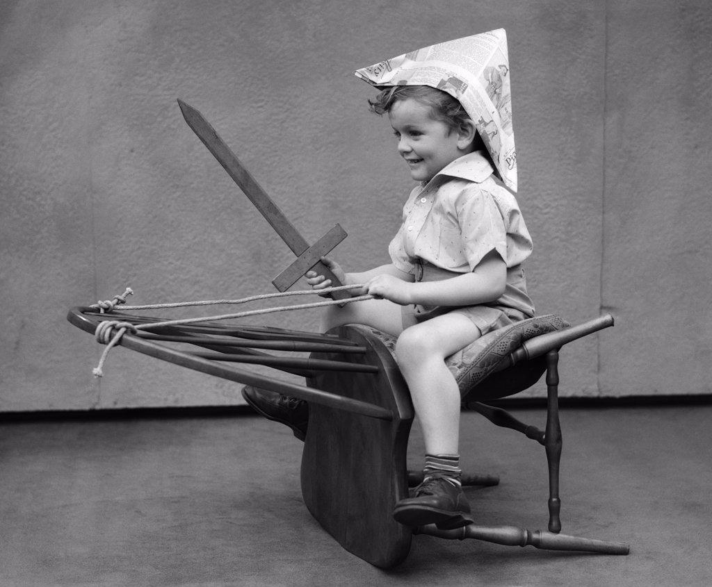 1930S Boy Playing Wooden Sword Paper Hat Riding Chair Like A Horse