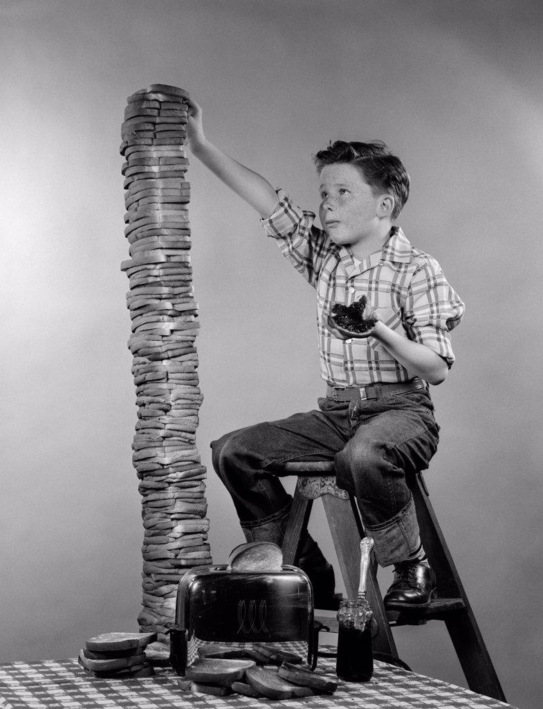 1950S Boy Eating Jelly Toast Sitting On Ladder Stacking Up Tall Pile Of Toast From Toaster