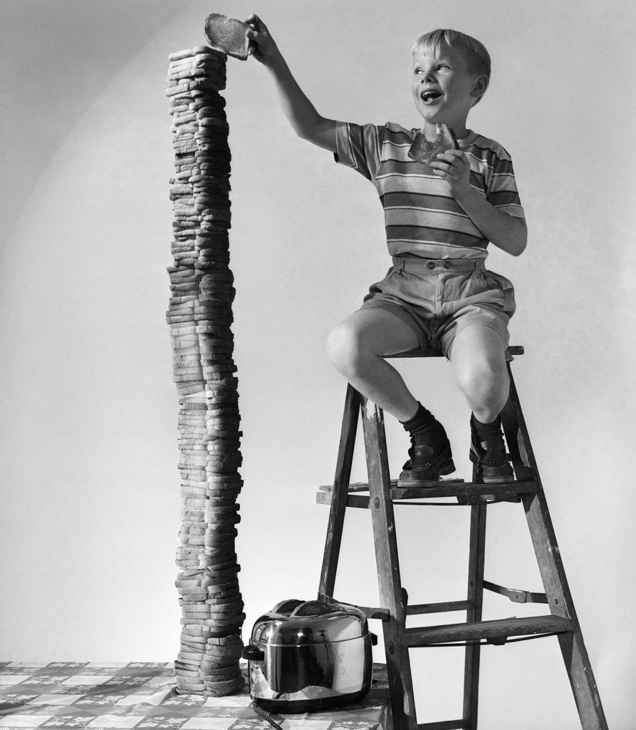 1950S Smiling Boy On Ladder Stacking Up Large Towering Pile Of Toasted Bread
