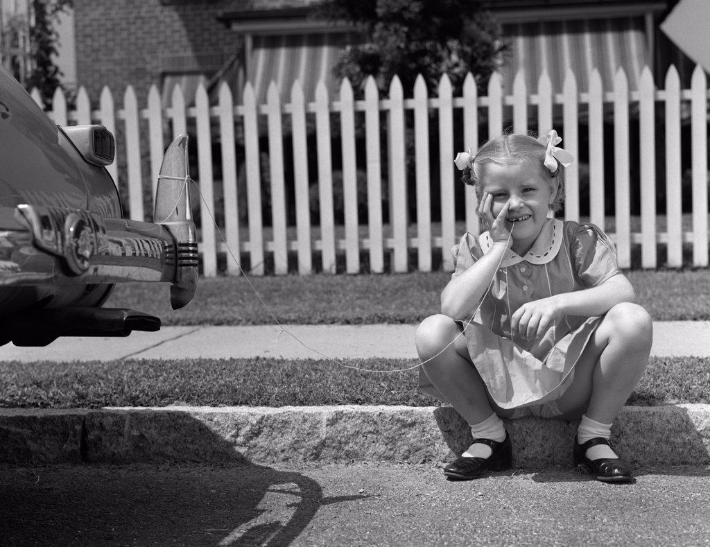 1940S Girl Sitting On Curb With Tooth Tied To Back Of Car Fender