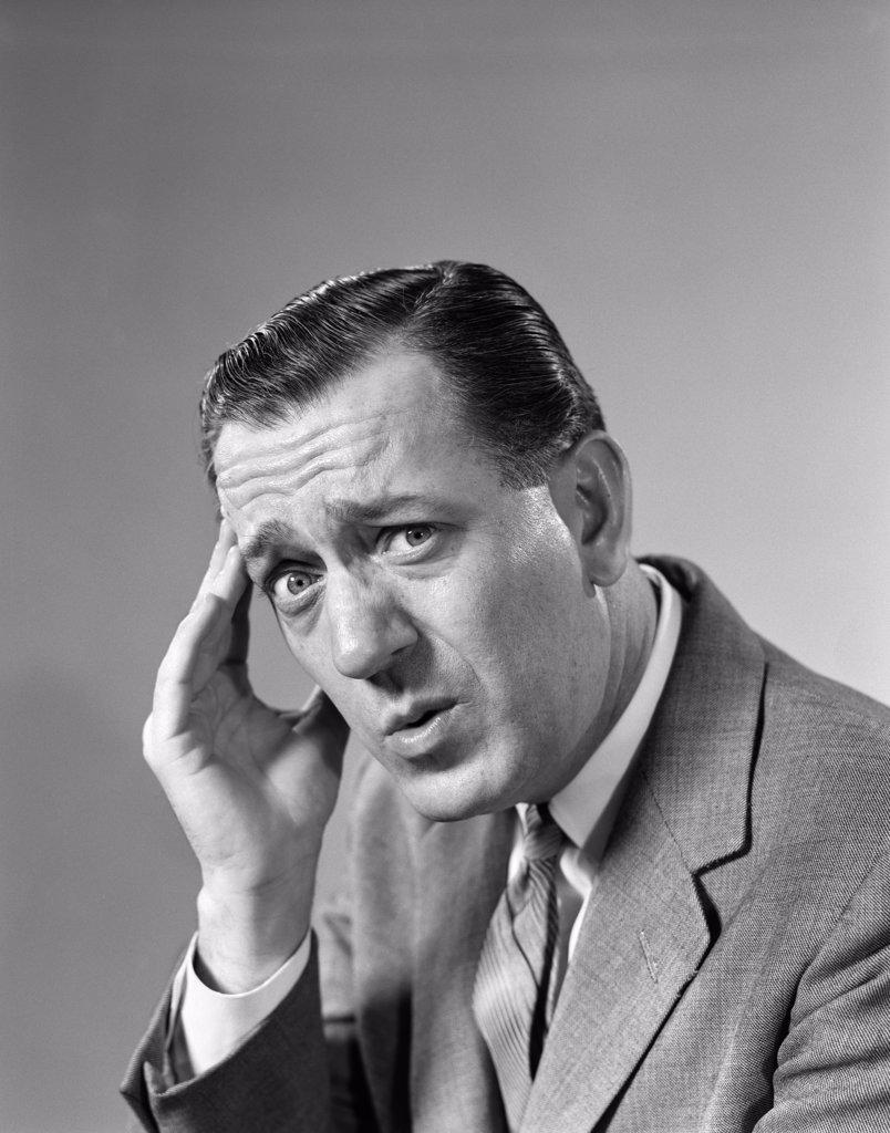 1960S Portrait Man In Suit And Tie With Wrinkled Brow Wincing And Holding Forehead Looking At Camera