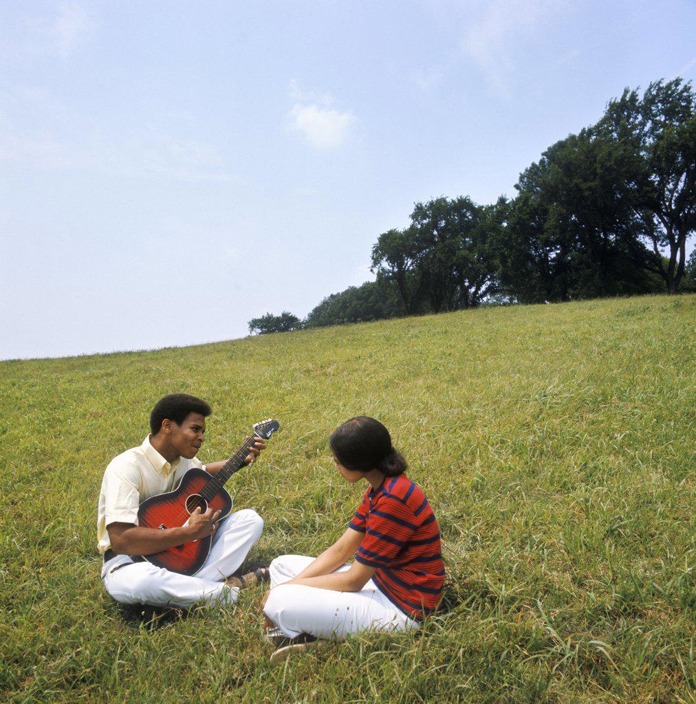 1970S Young African American Couple Sitting On Grassy Hill Man Playing Acoustic Guitar