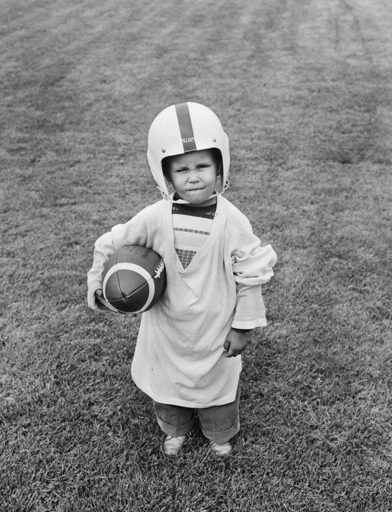 1950S Boy Standing In Grass Wearing Oversized Shirt & Helmet Holding Football
