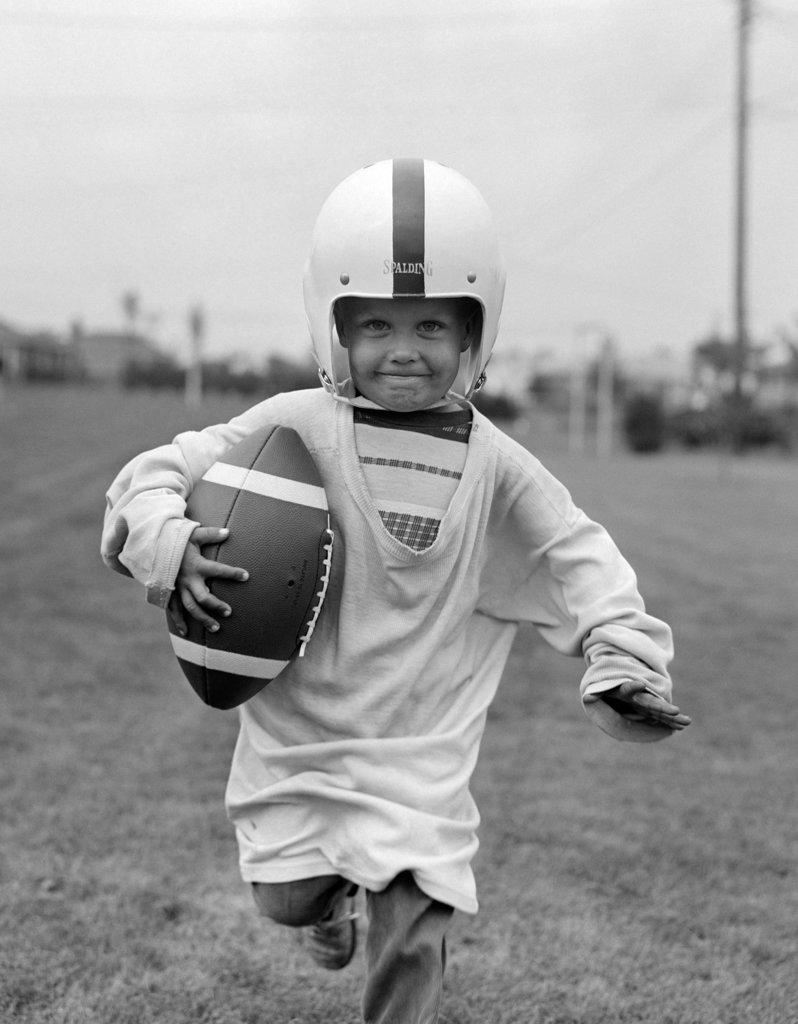 1950S Boy In Oversized Shirt & Helmet Running Toward Camera Holding Football