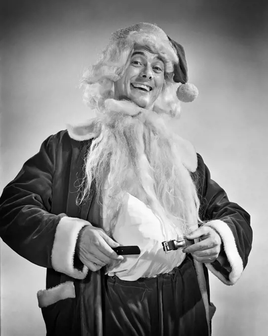 1950s SMILING MAN DRESSING UP IN SANTA COSTUME HOLDING BELT AROUND PADDED STOMACH