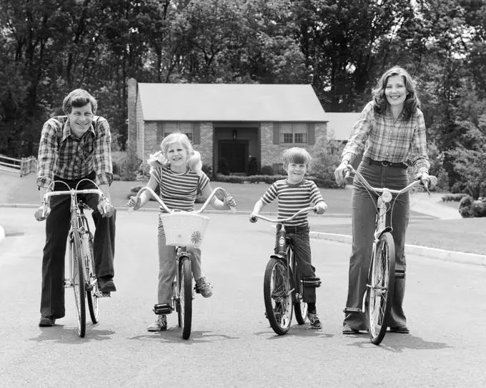 1970s SUBURBAN FAMILY OF FOUR SITTING ON BICYCLES LOOKING AT CAMERA