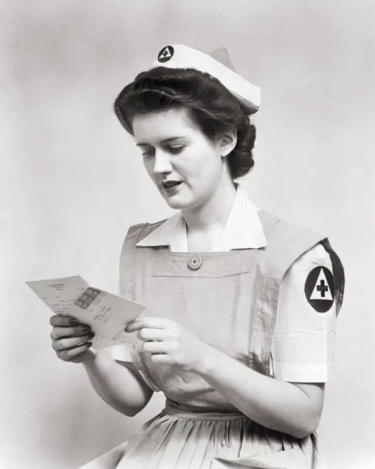 1940s WOMAN SERVING VOLUNTEER RED CROSS NURSE WEARING UNIFORM SMOCK DRESS AND CAP READING LETTER DURING WORLD WAR 2