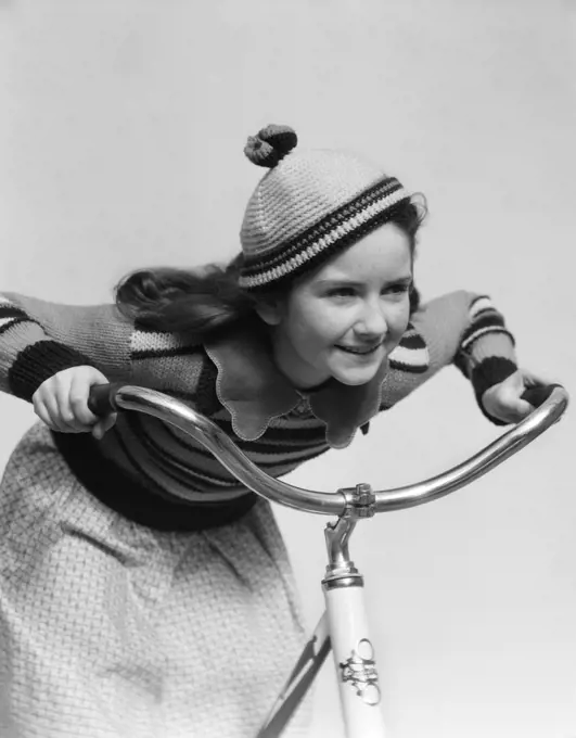 1930S Smiling Eager Little Girl In Knit Cap And Matching Sweater Riding Bike Leaning Into Handlebars