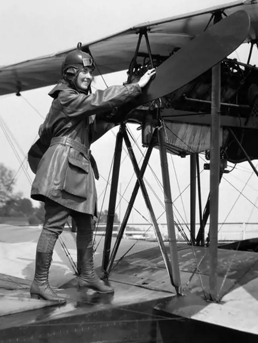 1920S Smiling Woman Aviator Turning Float Biplane Propeller Wearing Leather Flying Clothes Goggles And Helmet