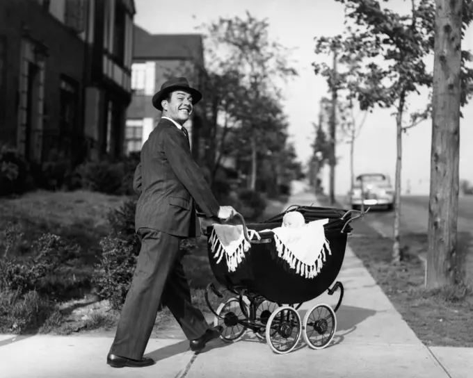 1940S 1950S Smiling Father In Suit & Hat Pushing Baby In Carriage Down Sidewalk