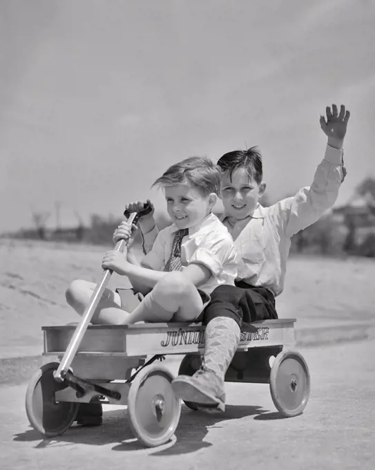 1930s TWO BOYS RIDING DOWN HILL IN JUNIOR ROADSTER WOODEN TOY WAGON BOY IN REAR WAVING LOOKING AT CAMERA
