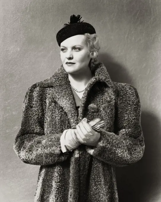 1930s 1940s UNSMILING BLONDE WOMAN WEARING BLACK PILLBOX STYLE HAT WITH TASSEL AND A GRAY PERSIAN LAMB FUR COAT LEATHER GLOVES
