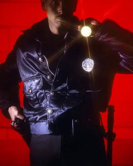 1990s POLICEMAN HAND ON GUN WITH FLASHLIGHT POINTED AT CAMERA RED BACKGROUND