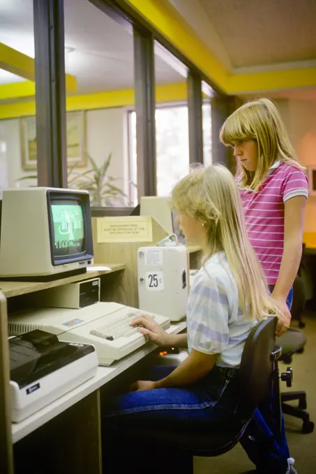 1980s 2 GIRLS WORKING ON COMPUTER IN PUBLIC LIBRARY COMPUTER LAB PAY AS YOU GO VENDING DEVICE
