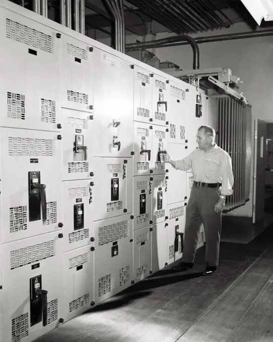 1960s MAN SUPERVISOR ENGINEER AT THE CONTROL PANELS OF MASSIVE AIR CONDITIONING SYSTEM FOR LARGE BUILDING
