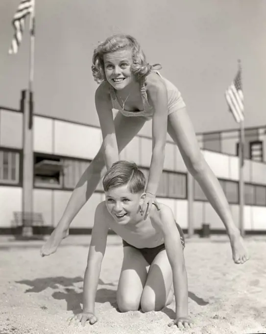 1930s 1940s SMILING GIRL AND BOY PLAYING LEAP FROG ON SAND BEACH BROTHER KNEELING BLONDE SISTER JUMPING OVER HIS BACK