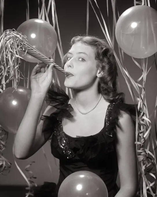 1940s 1950s PRETTY BRUNETTE WOMAN LOOKING AT CAMERA BLOWING A NEW YEAR PARTY NOISEMAKER AMID BALLOONS STREAMERS