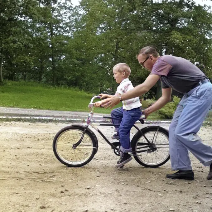 1960s MAN FATHER GIVING BOY SON ON BIKE A PUSH TEACHING HIM HOW TO RIDE BICYCLE