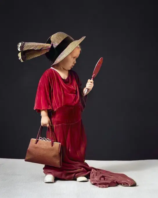 1930s 1940s CHARMING LITTLE GIRL PLAYING ADULT DRESS-UP MAKE-BELIEVE WITH HAT DRESS POCKETBOOK LOOKING AT HERSELF IN HAND MIRROR