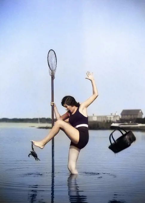 1920s WOMAN STANDING IN WATER CRABBING CARRYING BASKET AND NET ON A POLE SURPRISED BY CRAB BITING HER TOE