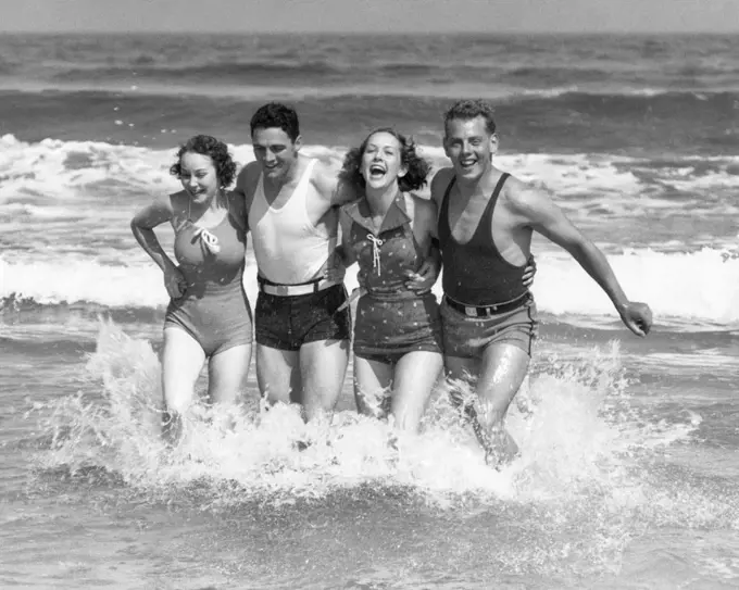 1930s TWO COUPLES MEN WOMEN LAUGHING RUNNING IN OCEAN SURF WAVES