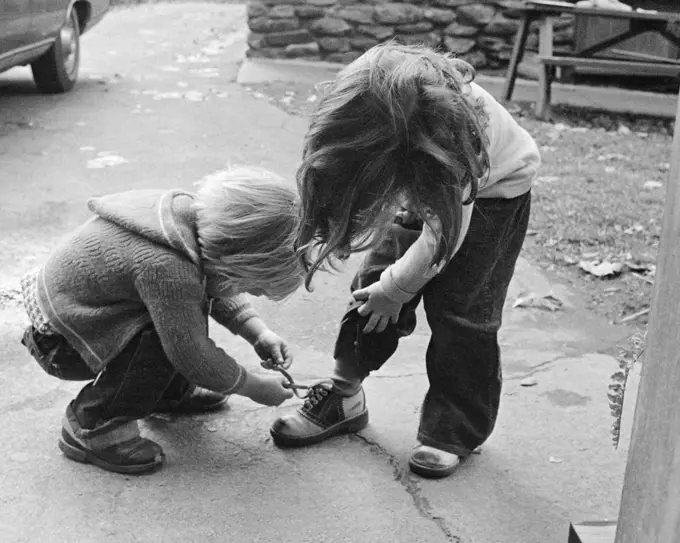1970s 1970s BLOND BOY BENDING OVER HELPING GIRL TIE HER SHOE 