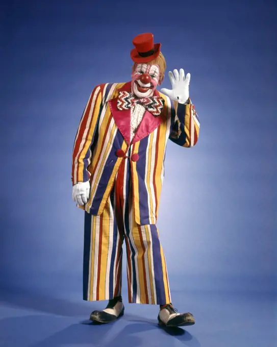 1970s HAPPY WAVING CIRCUS CLOWN STRIPED COLORFUL SUIT SMALL TOP HAT BIG BOW TIE FUNNY SHOES LOOKING AT CAMERA