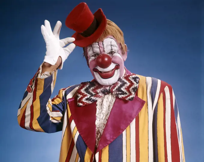 1970s PORTRAIT OF CLOWN IN STRIPED COSTUME TIPPING LITTLE RED TOP HAT