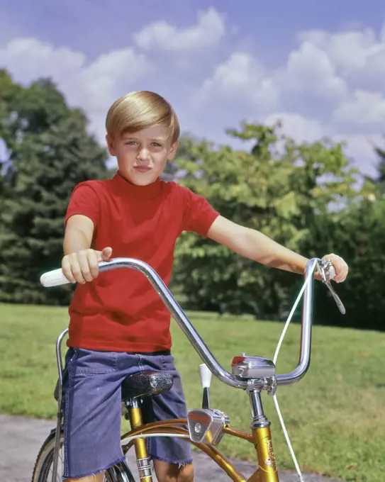 1960s PORTRAIT BOY BLOND WEARING RED SHIRT SITTING ON BIKE WITH PYRAMID CRUISER HANDLEBARS LOOKING AT CAMERA