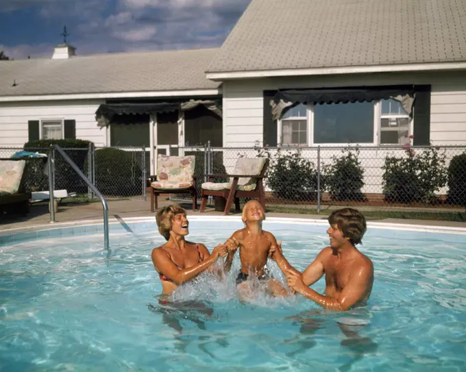 1970s FAMILY IN SUBURBAN BACKYARD SWIMMING POOL MAN WOMAN MOTHER FATHER PLAYING SPLASHING WITH LITTLE BOY SON