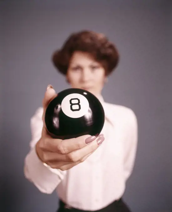 1970s WOMAN STANDING BEHIND HOLDING AN EIGHT BALL LOOKING AT CAMERA