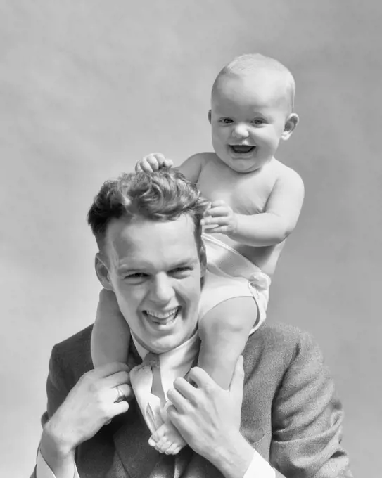 1930s LAUGHING FATHER CARRYING BABY SON ON HIS SHOULDERS AS KID PULLS DAD'S HAIR