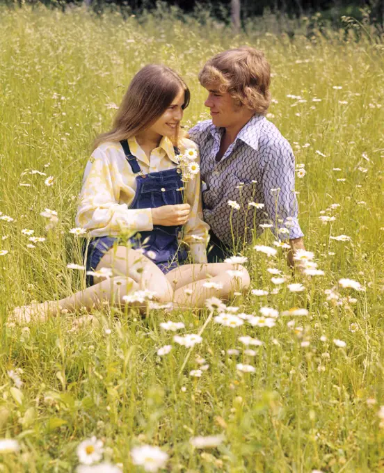 1970s ROMANTIC TEENAGE COUPLE SITTING IN A FIELD OF DAISIES
